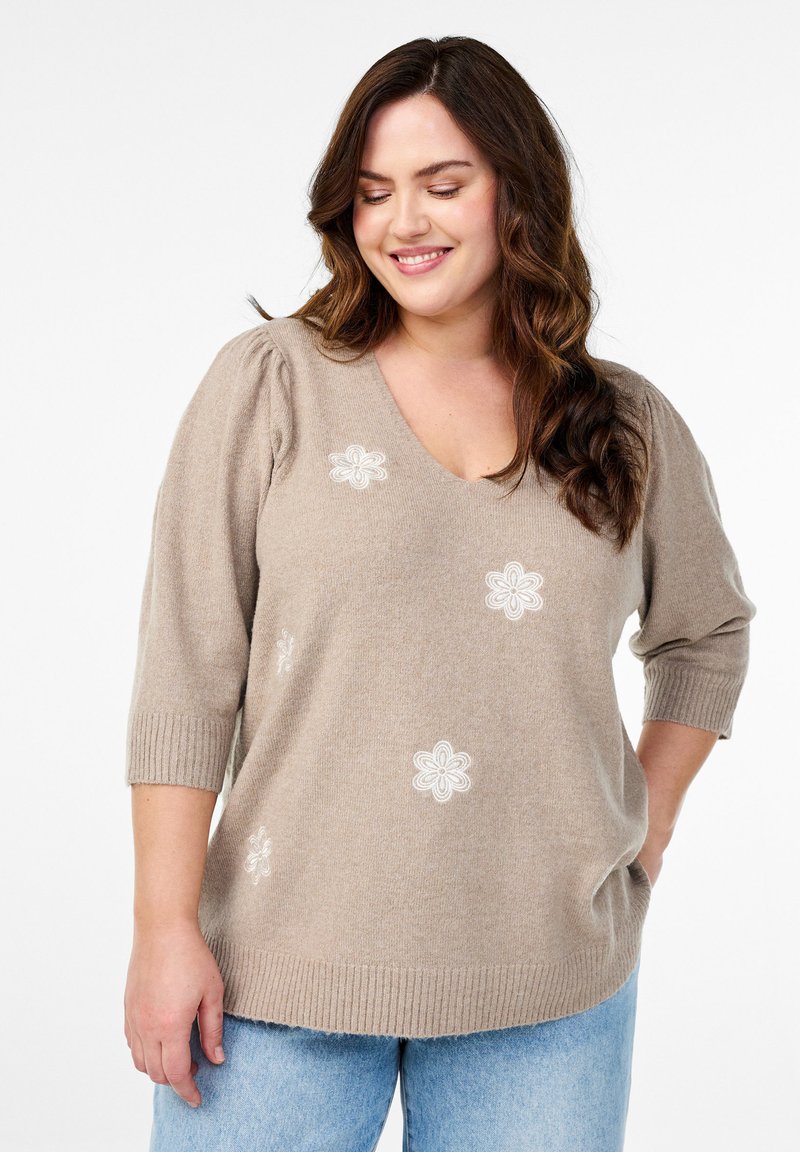 Maglione beige a maglia con scollo a V, maniche corte a palloncino e dettagli ricamati floreali bianchi. Tessuto morbido con orlo e polsini a coste.
