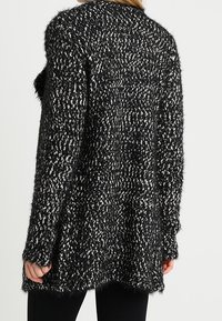 Czarny i biały, puszysty kardigan z luźnym krojem, długimi rękawami i nieco dłuższym tylnym dołem, z teksturowanym wzorem na całej powierzchni.