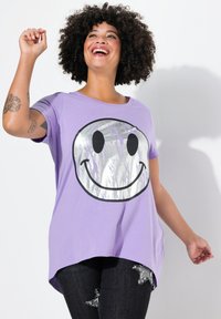 T-shirt violet à manches courtes avec un grand motif de visage souriant argenté. Tissu doux avec une coupe décontractée et un ourlet incurvé.