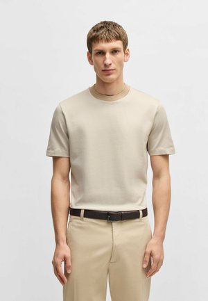 Beige Kurzarm-T-Shirt mit strukturierter Oberfläche und kontrastierendem hellbeigen Kragen, kombiniert mit hellbeigen Hosen und einem braunen Gürtel.