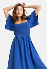 Vestido azul de escote cuadrado con corsé fruncido y mangas anchas y cortas. Hecho de un tejido ligero con una falda fluida. Sin estampados ni adornos.