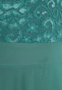 Tissu bleu sarcelle avec un motif de dentelle florale en haut et un textile lisse et uni en dessous, séparés par une bande horizontale.