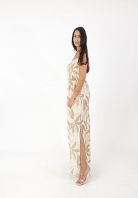 Robe maxi en beige clair avec un imprimé botanique dans des verts et des roses doux. Dotée d'une taille élastique, de poches latérales et d'une fente haute jusqu'à la cuisse.