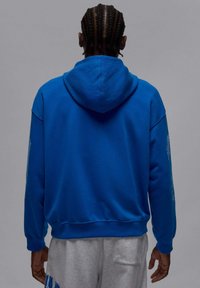 Niebieska bluza z kapturem o gładkiej fakturze, z kieszenią kangura i ściągaczami na rękawach. Uzupełniona subtelnymi detalami na rękawach.