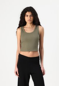 Olivově zelený rozšířený crop top s širokými ramínky, který má přiléhavý střih a jemnou texturu, spárovaný s volnými černými kalhotami.