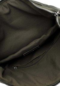 Interno di una borsa in tessuto khaki con una texture liscia, evidenziato da una tasca con zip e un dettaglio di cucitura a contrasto lungo le cuciture.