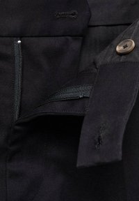 Black fabric detail showing a zippered pocket, button, and stitching. Smooth texture with a clean design and hidden fastening elements.
