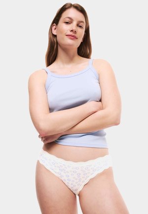 Top de tirantes azul claro combinado con un tanga blanco con encaje y un patrón floral. La modelo está de pie con los brazos cruzados, mirando hacia adelante.