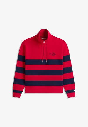 Rød pullover med lange ærmer med marineblå vandrette striber, kvart lynlås krave og lille skriftslogo på venstre bryst.