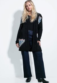 Czarny sweter dzianinowy z wzorami w blokach kolorystycznych w niebieskim i kremowym kolorze. Zestawiony z dżinsowymi spodniami o szerokich nogawkach i czarnymi botkami za kostkę.