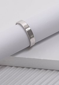 Silberner Bandring mit glatter, polierter Oberfläche, flachem Design und abgerundetem Innenrand, präsentiert auf einem weißen zylindrischen Objekt.