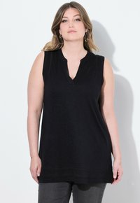 Tunic nera senza maniche con scollatura a V e spacchi laterali, caratterizzata da una texture liscia e una vestibilità ampia che si adagia sui fianchi.