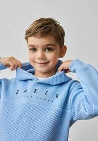 Jasnoniebieska bluza z kapturem z teksturowanym dolnym panelem i gładką górą. Posiada wzorzysty kaptur oraz ciemny tekst "BAKER by TED BAKER."