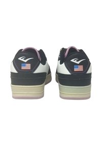 Sneaker bianco e nero con tomaia in pelle texture, accenti pastello e una piccola bandiera americana sul tallone. Suole piatte di colore chiaro.