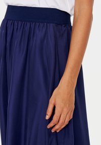 Laivonsininen hame, jossa on leveä joustovyötärö, pehmeästä ja valuvalta kankaalta, joka on sileä tekstuuriltaan, kerätty vyötärölle rentoa istuvuutta varten.