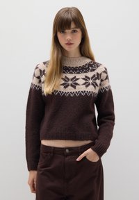 Bruine gebreide trui met een crèmekleurig en donkerbruin geometrisch patroon op de schouderstukken, ribgebreide manchetten en een cropped ontwerp. Gemaakt met bijpassende bruine broeken.