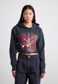 Cropped black hoodie with red graphic '28' and white stars. Features a drawstring hood and ribbed cuffs, paired with high-waisted dark jeans.