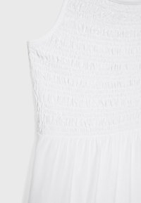 Weißes ärmelloses Kleid mit gerafftem Oberteil und fließendem Rock, aus leichtem Stoff mit glatter Textur gefertigt.
