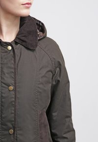 Dark green jacket with a corduroy collar, gold snap buttons, and side pockets. Features a plaid interior lining and a smooth texture.