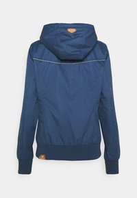 Marinblå huvjacka med en slät yta, elastiska muddarna och en brun logotyp patch vid fållen. Har grå sömmar längs ryggen.