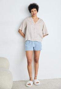 Lichte beige, gemusterde,短 mouwen overhemd gecombineerd met lichtblauwe shorts en witte fluffy slippers. Gladde textuur, ontspannen pasvorm.