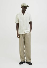 Chemise claire à manches courtes avec de subtiles rayures, associée à un pantalon large beige et des chaussures noires, complétée par une casquette verte.