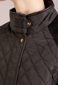 Quiltad mörkgrå jacka med svart läderkrage, guldfärgade tryckknappar och diagonalt sömnadsmönster.