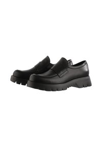 Chaussures noires en cuir à enfiler avec une semelle épaisse et texturée, dotées d'une large sangle à l'avant et d'un design à bout rond.