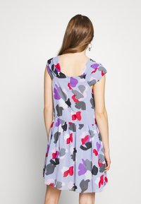 Ljusblå blommig klänning med korta ärmar, med färgglada abstrakta mönster i rött, lila, svart och rosa; figurnära överdel och utsvängd kjol.