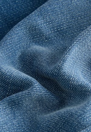 Tessuto di denim, blu medio con una superficie morbida e testurizzata. Presenta leggere variazioni di colore e il classico motivo tessuto tipico del denim.