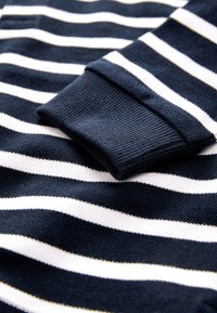 Bavlnený sveter s námorníckym modrým a bielym vodorovným pruhovaným vzorom, s hrubým rebrovaným manžetovým lemom a hladkým povrchom látky.