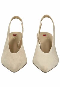 Zapatos de tacón destalonados de ante beige con punta afilada. Presentan una textura suave, un diseño minimalista y un sutil detalle del logo dorado en la plantilla.
