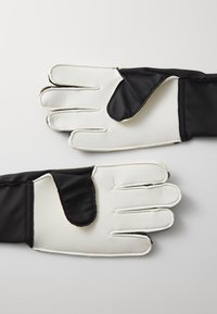 Gants de gardien noir et blanc avec une surface lisse et rembourrée. Les paumes sont blanches avec une prise texturée ; le dos est en tissu noir ajusté.