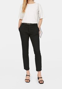 Witte kortekorte mouwen shirt, zwarte op maat gemaakte broek, zwarte riem en zwarte strap heels. Minimalistisch ontwerp zonder zichtbare patronen of accenten.
