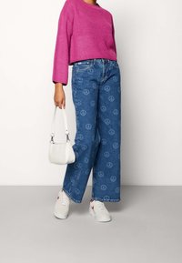 Rosa stickad kort tröja, blå denim vida byxor med fredssymbolsmönster, vit handväska och vita sneakers med röda accenter.