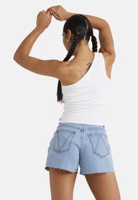 White one-shoulder tank top and blue denim shorts with frayed hem. Shorts feature two back pockets with V-shaped stitching detail.