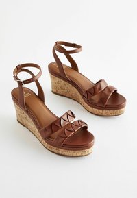 Sandali wedge marroni con piattaforma in sughero, due fasce larghe con design a scallop e cinturini alla caviglia regolabili. Tessuto in pelle liscia.