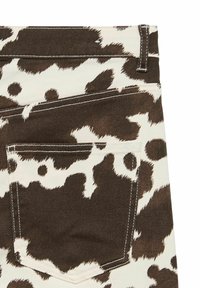 Denim tkanina s uzorkom smešane smeđe i bele krave, prikazujući detalje zadnjeg džepa, sa kontrastnim šavovima i teksturiranim završetkom.