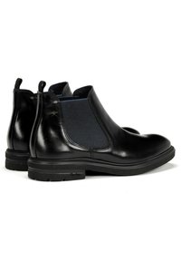 Botas Chelsea de cuero negro con paneles laterales elásticos, punta redonda y acento texturizado en azul marino. Suela de goma plana para estabilidad y agarre.