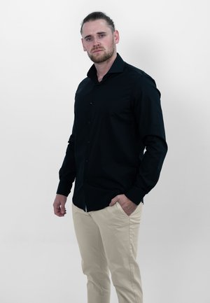 Zwarte blouse met lange mouwen en knoopsluiting aan de voorkant, in een getailleerd ontwerp, gecombineerd met lichtbeige broeken. Glad textuur, geen zichtbare patronen.