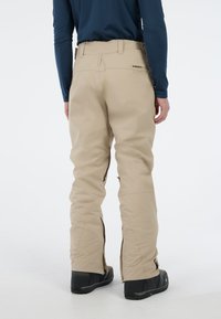 Beige sneeuwbroeken met een rechte snit, gemaakt van stevig materiaal, met zijrits en een gebrandmerkte tailleband, gecombineerd met zwarte laarzen.