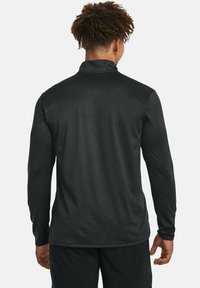 Schwarzes Langarmshirt aus leichtem, strukturiertem Stoff. Verfügt über einen hohen Kragen und ein Logo im oberen Rückenbereich für zusätzliche Details.