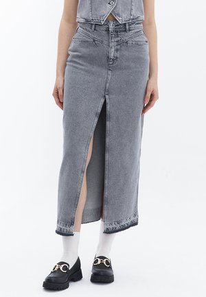 Grijze denim maxi-rok met een vooruitsnijding, een rafelige zoom en een sluiting met bovenste knoop. Gepaarde met zwarte loafers en witte sokken.