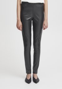 Leggings en simili cuir noir avec une texture lisse, fit slim, taille haute et sans coutures visibles. Associés à des ballerines noires à bouts pointus.