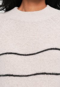 Helles rosa gestricktes Sweatshirt mit rundem Ausschnitt und schwarzen wellenförmigen Streifen auf der Vorderseite. Weiche Textur mit lockerer Passform.