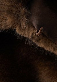 Brązowa tkanina o miękkiej, futrzastej fakturze na krawędzi, z małym brązowym zapięciem do zamykania.