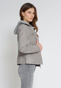 Grijze leren jack met een capuchon, met een glanzende afwerking, ritssluitingen en zijzakken. Draagt over grijze slim-fit jeans.