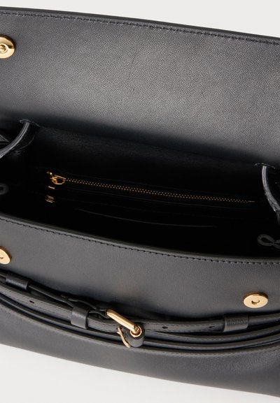 Sac à main en cuir noir ouvert pour montrer l'intérieur avec une poche zippée et des détails en métal doré.