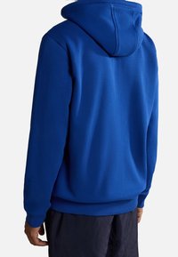 Blå hættetrøje med snørelukning, ribbede manchetter og kant. Stoffet er en glat blanding af bomuld. Simpelt design uden synlige logoer eller mønstre.