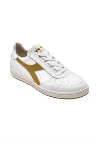 Sneaker bianco in pelle con dettagli perforati, accenti dorati e design senza lacci. Suola in gomma con battistrada marrone chiaro.